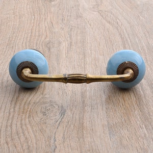 May include: A light blue ceramic drawer pull with a brass finish. The pull has a rounded shape and a decorative design on the front.