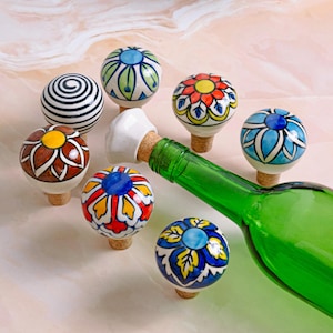 May include: Set of seven colorful ceramic bottle stoppers with various floral and geometric designs. The stoppers are made of white ceramic with a cork base and feature vibrant colors like red, blue, yellow, and green.