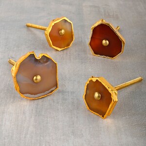Może przedstawiać: Cztery agatowe gałki do szuflad z złotymi metalowymi akcentami. Agat jest w odcieniach brązu, pomarańczy i bieli.