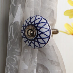 Könnte beinhalten: Weißer und blauer Vorhang-Halter aus Keramik mit geometrischem Muster. Der Halter hat einen Metallhaken.