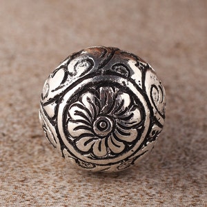 May include: A silver metal bead with an intricate floral design. The bead is round and has a smooth surface.