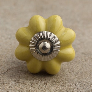 May include: A yellow ceramic flower-shaped cabinet knob with a silver center.