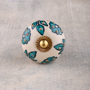 May include: White ceramic knob with a floral design in shades of teal and gold. The knob has a raised gold center.