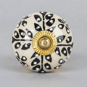 May include: White ceramic knob with a black and white floral pattern and a gold metal center.