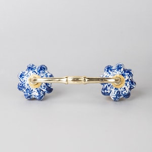 May include: A blue and white ceramic cabinet pull with a gold metal bar connecting two flower-shaped knobs.