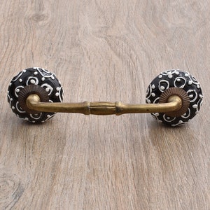 May include: Black and white ceramic drawer pull with a brass bar connecting the two knobs. The knobs have a circular shape and a white and black geometric pattern.