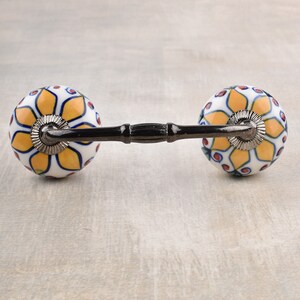 Può includere: Un paio di pomelli per cassetti in ceramica con un design floreale giallo, blu e rosso. I pomelli sono fissati a una barra di metallo.