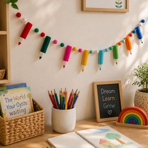 May include: A felt garland featuring miniature pencil shapes in red, dark green, pink, yellow, blue, light green, and orange, interspersed with small white, red, and green felt balls, hanging horizontally against a plain wall.
