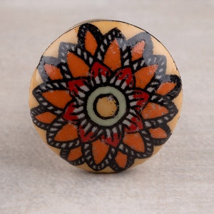 Può includere: Un pomello rotondo in ceramica con un design floreale colorato. Il pomello presenta un grande fiore arancione con contorni neri e accenti rossi su uno sfondo crema.