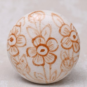 May include: A white ceramic sphere with a brown floral design. The sphere has a smooth, textured surface and is decorated with a repeating pattern of stylised flowers.
