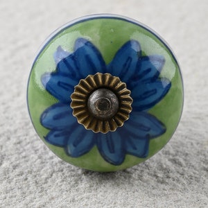 May include: A green ceramic knob with a blue flower design and a brass knob in the center.