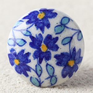May include: A white ceramic knob with a blue and yellow floral design. The knob is round and has a smooth surface.