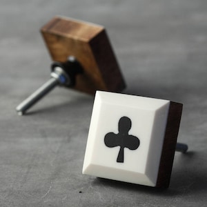 May include: Two square cabinet knobs with a wood and white finish. One knob features a black clover design.