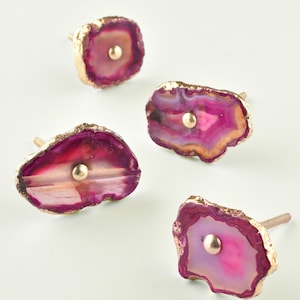 Op de afbeelding: Vier roze agaat-ladegrepen met gouden afwerking. Elke greep heeft een kleine gouden knop in het midden.