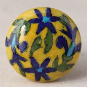 May include: A yellow ceramic knob with a blue and green floral design. The knob is round and has a smooth surface.