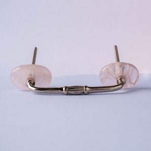 May include: A silver drawer pull with two round, translucent pink knobs. The knobs are made of rose quartz.