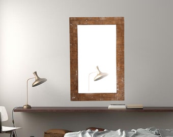 May include: A rectangular mirror with a woven brown frame hangs on a white wall. A modern, gold-toned lamp with a curved arm and a conical shade is positioned to the left. A second lamp is reflected in the mirror.
