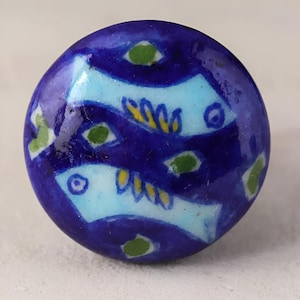 Könnte beinhalten: Ein blauer Keramik-Knopf mit einem weißen und gelben Blumenmuster. Der Knopf hat eine glänzende Oberfläche und ist mit grünen und gelben Akzenten verziert.