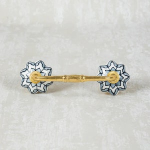 May include: A pair of ceramic drawer pulls with a gold metal bar connecting them. The ceramic pulls are white with a blue and black geometric pattern.