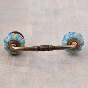 May include: A blue and yellow ceramic drawer pull with a brass arch and a decorative knob on each end.