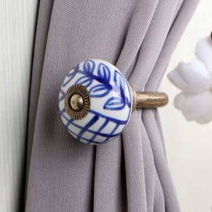 以下が含まれることがあります： 花柄の青と白のセラミック製のカーテン留め。留め具は金属製のフックに取り付けられています。