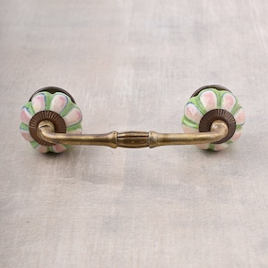 Könnte beinhalten: Ein Messing-Schubladengriff mit zwei Keramikknöpfen. Die Knöpfe sind grün, rosa und weiß mit einem floralen Muster.