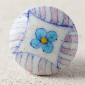 May include: A white ceramic knob with a blue flower and pink and blue stripes.
