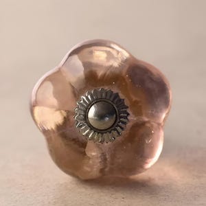 Pode incluir: Um botão de armário de vidro rosa com um centro de metal prateado.