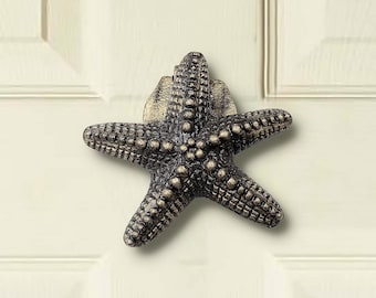 May include: A bronze starfish door knocker with a textured surface. The knocker is mounted on a white door.
