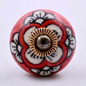 Handgemaakte keramische kastknop met bloemenmotief in koraalrood, wit en zwart.