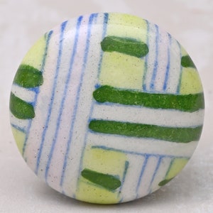 May include: A round ceramic knob with a white background and a geometric pattern of green, blue, and yellow lines.