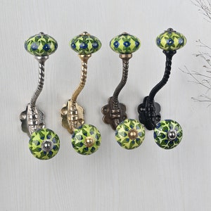 May include: Four wall hooks featuring a twisted metal arm and a decorative ceramic knob at the top and bottom. Each knob is painted with a green leaf pattern and small blue flowers. The metal bases and arms come in silver, gold, bronze, and black.