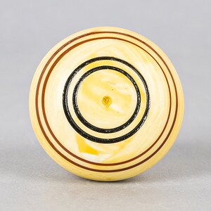 May include: A round, cream-colored game piece with black and brown concentric circles.