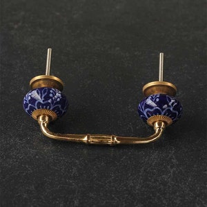May include: A pair of blue and white ceramic drawer pulls with a gold metal connecting bar. The ceramic knobs have a floral pattern.