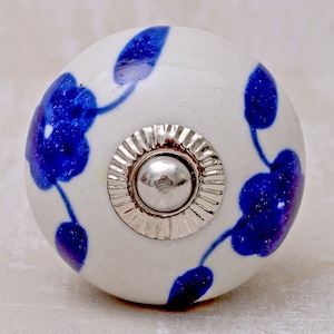 Può includere: Pomo in ceramica bianca con un motivo floreale blu e un accento in metallo argentato. Il pomo è rotondo e ha una superficie liscia.