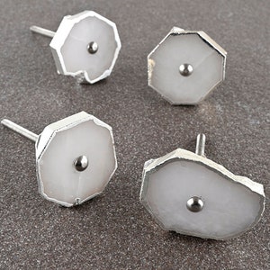 Op de afbeelding: Set van vier witte agaat-kastknoppen met zilveren metalen accenten. Elke knop heeft een unieke, onregelmatige vorm en een kleine zilveren metalen bol in het midden.