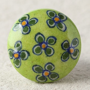 May include: A green ceramic knob with a floral design. The knob features five blue and green flowers with yellow centers.