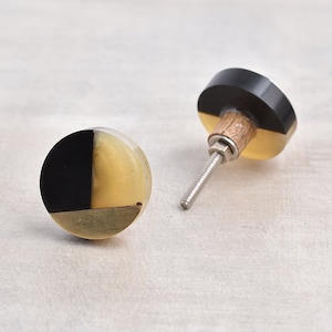 May include: Two round cabinet knobs with a black and cream design. The knobs have a wood base and a silver screw.