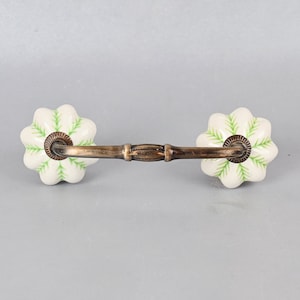 May include: White ceramic drawer pull with a green floral design and a bronze metal bar.