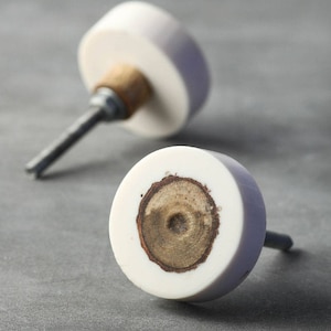 Könnte beinhalten: Zwei weiße Keramik-Schrankknöpfe mit Holzeinlage. Ein Knopf hat eine sichtbare Schraube.