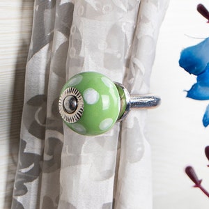 Puede incluir: Atado de cortina de cerámica verde con lunares blancos y un anillo de metal plateado.