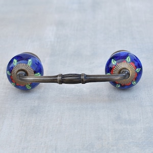 Puede incluir: Un tirador de cajón de cerámica azul y rojo con un diseño floral y un acabado en latón.