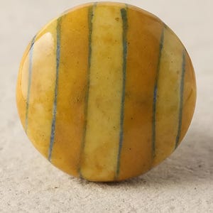 Puede incluir: Un pomo redondo de cerámica rayado en amarillo y azul. El pomo tiene un acabado brillante y es perfecto para añadir un toque de color y estilo a cualquier armario o cajón.