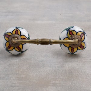 May include: A pair of ceramic drawer pulls with a floral design in shades of yellow, red, green, and blue. The pulls are attached to a brass bar.
