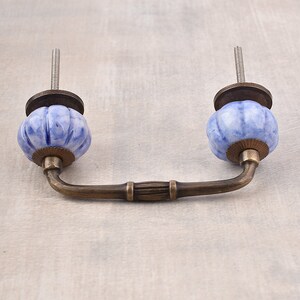 Pode incluir: Uma maçaneta de armário de cerâmica azul e branca com uma alça de arco de latão.