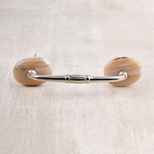 May include: A silver cabinet pull with two round, beige and white agate knobs.