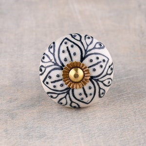 May include: White ceramic knob with a black floral design and a gold metal center.
