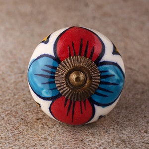 May include: A ceramic knob with a floral design in shades of red, blue, and yellow. The knob has a brass center with a decorative ring.