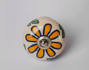 Pode incluir: Um botão de cerâmica branca com uma flor amarela e folhas verdes pintadas sobre ele. O botão tem um parafuso de metal prateado no centro.