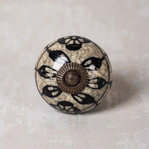 May include: A round ceramic knob with a black and white floral design and a brass accent. The knob has a speckled, textured surface.